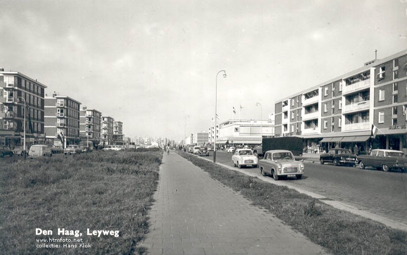 Foto: de Leyweg in de '60er jaren. Het witte gebouw met de vlaggen is van V&D. De Gruyter zat iets links van de zwarte auto op de foto. Albert Heijn net buiten beeld, rechts. In de jaren '80 is de Leyweg verbouwd. Afgesloten voor doorgaand verkeer. De groenstrook op de foto, het fietspad en het wegdek zijn volgebouwd met winkels.